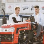 Two men in casual attire inspecting red tractors in an outdoor showroom.
