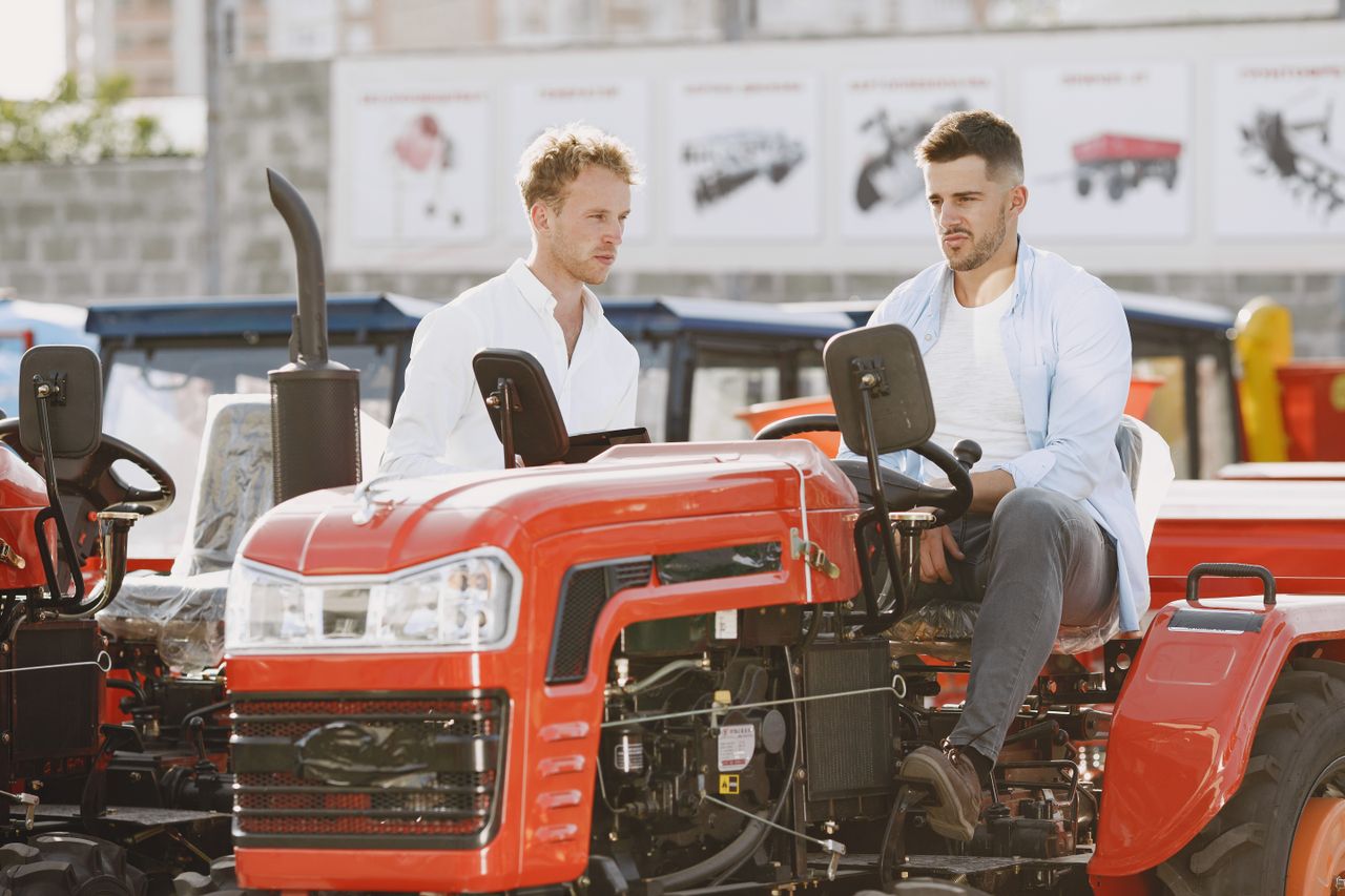 Two men in casual attire inspecting red tractors in an outdoor showroom.